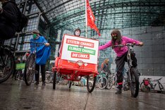 Drei Teilnehmende mit ihren Rädern auf einem Klimastreik. Das eine Rad ist ein Lastenrad auf dem vorne prangt "System change not climate change. Die Linke".
